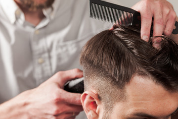 The hands of barber making haircut to young man in barbershop