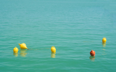 Fototapeta na wymiar Five bright yellow and orange marker buoys floating in blue turquoise lake water, Balaton, Hungary. Abstract composition of water safety.