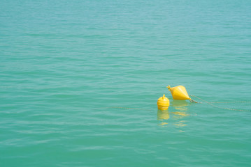 Two bright yellow marker buoys floating in blue turquoise lake water, Balaton, Hungary. Abstract composition of water safety.