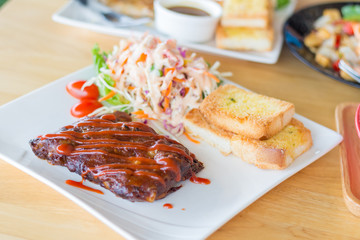 Close up view of pork barbecue ribs with barbecue sauce that served with garlic bread and vegetable salad.