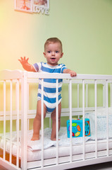 1 year old child waving his hand standing in his crib
