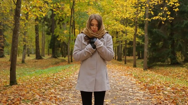 Charming young woman stands and shivers from cold in an autumn park