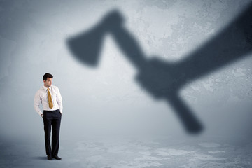 Fototapeta premium Businessman afraid of a huge shadow hand holding an axe concept