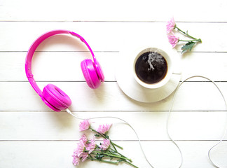 Pink Headphones and coffee cup on wooden desk table with pink flower. Music  and lifestyle concept. Top view with copy space