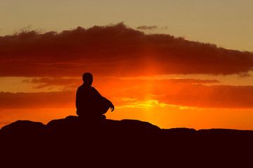 Guy meditating at sunset sitting on a rock by the sea