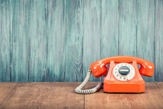 Old orange retro rotary telephone on table front grunge textured wooden wall background. Vintage instagram style filtered photo