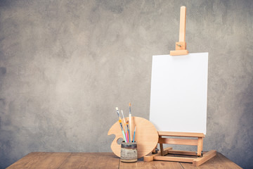 Portable desk easel for painting with canvas blank, brushes and artist's palette on wooden table...