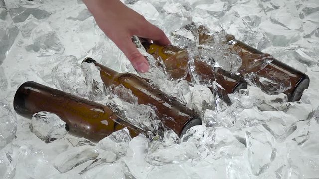 Man's hand pulls one bottle from the ice. White background. Slow motion
