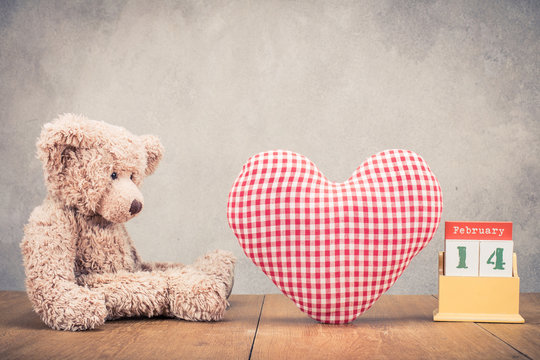 Retro Teddy Bear toy, red and white heart shape, desk calendar with 14th of February date front concrete wall background. Vintage instagram old style filtered photo