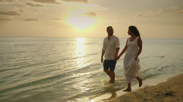 Romantic couple in love walking by the sea at sunset. Honeymoon and vacation by the sea concept