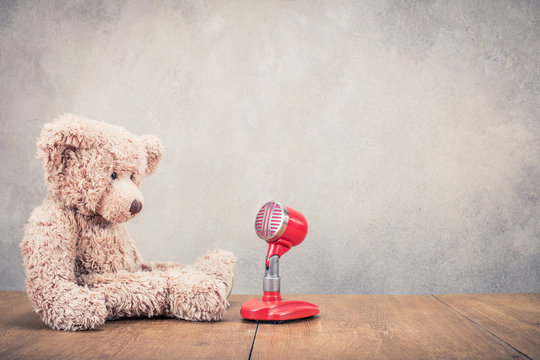 Retro Teddy Bear toy with red microphone front concrete textured wall background. Vintage old instagram style filtered photo