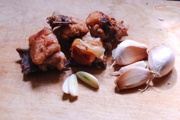  Roast from chicken meat on bones with cloves of garlic on a light background