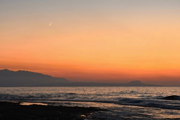 Beautiful summer sunset by the sea. Amazing scenery on the beach with waves and reflection of the sun. Background for holiday and vacation travel. Greece Crete Island.