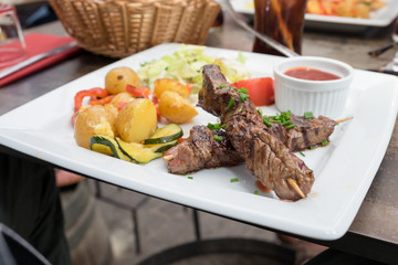 Grilled meat skewers served with baked potatoes and hot chili sauce in the restaurant of Carcassonne, France