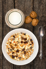 White bowl with Granola or Muesli and a jar of milk or plain yogurt with a spoon on a vintage wood background. Healthy breakfast top view composition