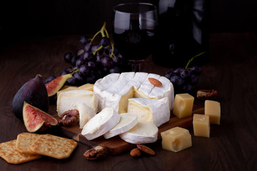 Variety of different cheese with wine, fruits and nuts. Camembert, goat cheese,  gauda,  emmental