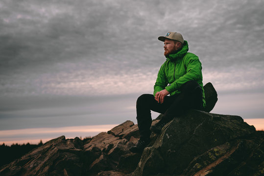 Wanderer sitzt auf einem Felsvorsprung im Harz bei Sonnenaufgang