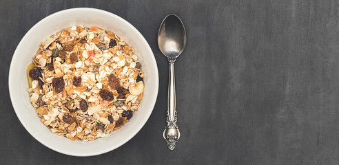 White bowl with Granola or Muesli and a spoon on a stone or marble background. Healthy breakfast composition with copy space