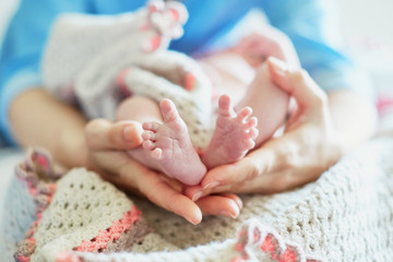 Obraz na płótnie Canvas Mother holding newborn baby's feet in her hands