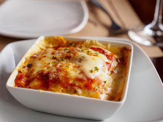 Close-up detail of a bolognese lasagna dish on white porcelain dishes at an Italian restaurant. Food and cusine concept.