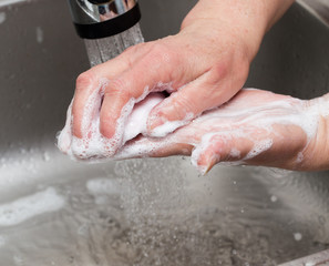 Fototapeta premium Woman washes her hands with soap under a tap of water