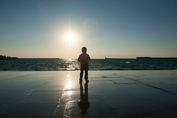 little boy watching the sea against the sunset