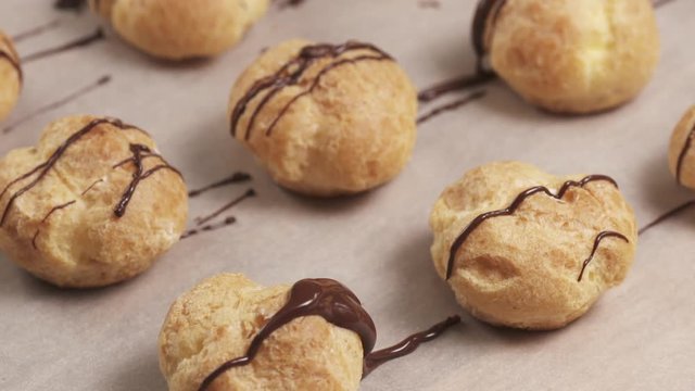 Slow motuion decorating profiteroles with fine dark chocolate on parchment paper