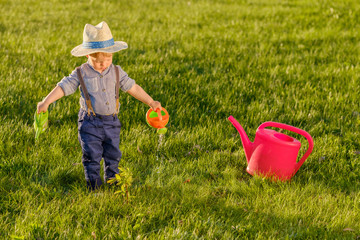 Toddler child outdoors. One year old baby boy wearing straw hat using watering can © haveseen