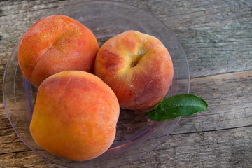 Three ripe peaches with green leaves in a plastic plate on the old wooden background