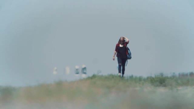 Young stylish girl in cowboy clothes doing hitch-hiking in desert, on the road. She carries backpack and hat. Pass trucks, delivery trucks. California or Nevada. Search yourself, escape from problems