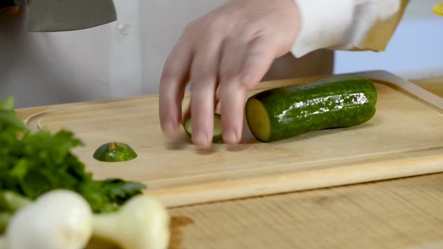 Hands of the cook knife big kitchen a fresh green cucumber on a chopping board from a tree
