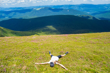 Fototapeta na wymiar Young woman hiker lies on the top of hill and Enjoy beautiful mountain valley view in summer day. Freedom concept
