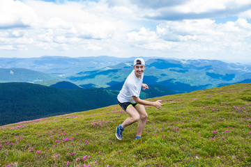 Young happy guy having fun on the top of the hill, the mountains on background