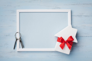 Miniature white house decorated red bow ribbon, frame and keychain on blue wooden background....