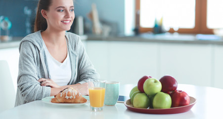 Young woman with orange juice and tablet in kitchen