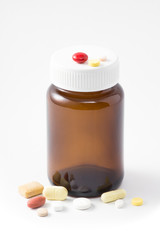 the empty light brown bottle has some scratch with various drug pills on white background