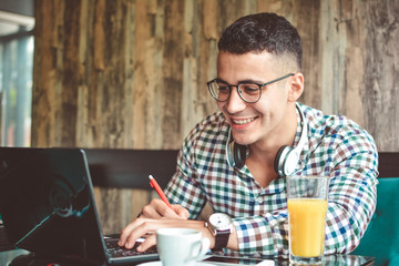 Handsome young businessman is using a tablet and smiling, sitting at bar counter in a modern urban cafe