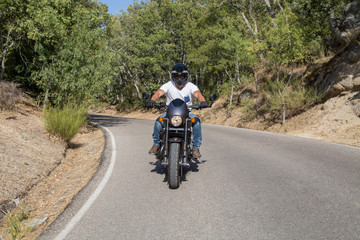 Young man riding a motorcycle on road in mountains in sunny day.  
