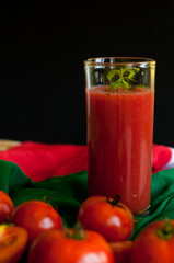 Glass and bottle of tomato juice with vegetables and green napkin on wooden background
