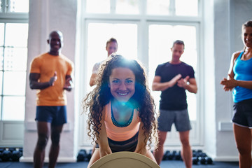 Smiling woman weightlifting with friends clapping in the backgro