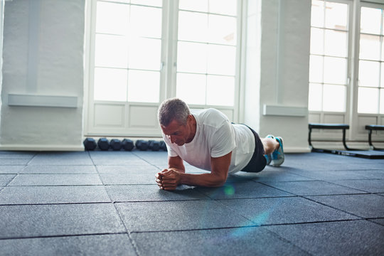 Mature man in sportswear planking on a gym floor