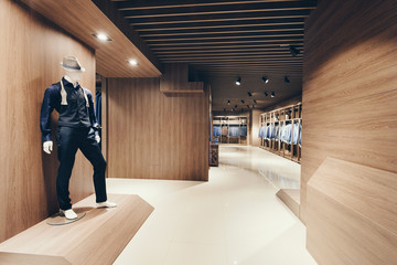Interior of a clothing store and business suits. Wall covering under a tree. In the foreground there is a maniken in a suit and hat. - obrazy, fototapety, plakaty
