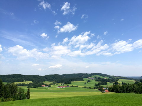 Aufziehende wei&szlig;e Wolken &uuml;ber gr&uuml;ner Weidelandschaft im Sommer bei blauem Himmel und Sommenschein im Pfaffenwinkel im sch&ouml;nen Oberbayern in Rudersau bei Rottenbuch im Kreis Weilheim-Schongau