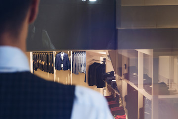man in a business suit looks toward the shelves in the distance in a boutique of clothes. View from behind the shoulder, shallow depth of field