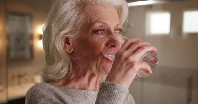 Close up of attractive elder woman swallowing capsule washing it down with water. Older woman in her 50s taking pill inside bathroom to maintain health smiling. 4k 