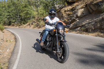 Side view of man sitting on parked custom motorcycle on road in mountains. 