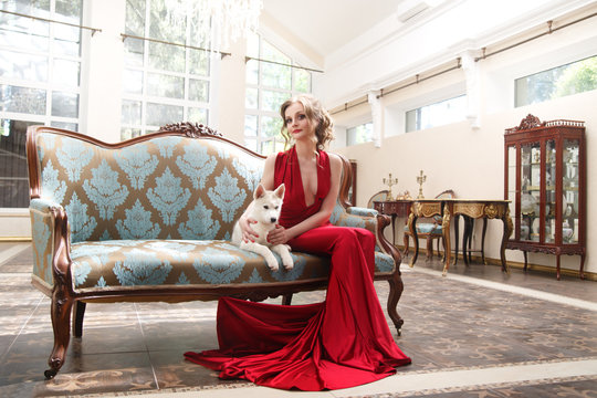 Beautiful woman in an elegant red dress with a cute puppy dogs of the Husky breed in a classic interior.