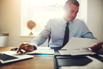 Smiling executive reading documents and working on a laptop