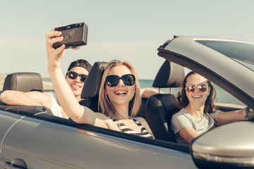 Happy friends taking selfie in car