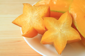 Closed up pair of vibrant yellow sliced ripe Star Fruits on white plate served on wooden table 